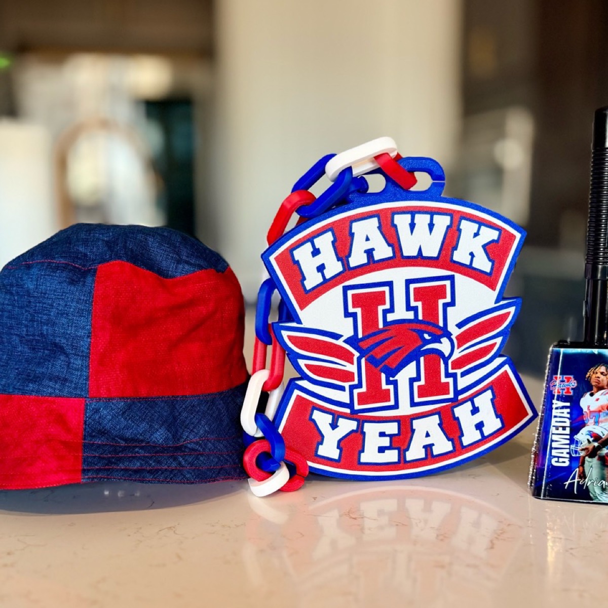 Red and navy custom fan hat displayed beside a Hays Hawks chain and personalized cowbell.