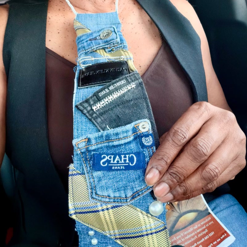 Handmade necktie assembled from layered blue denim, plaid fabric, pockets, and pearl-like accents